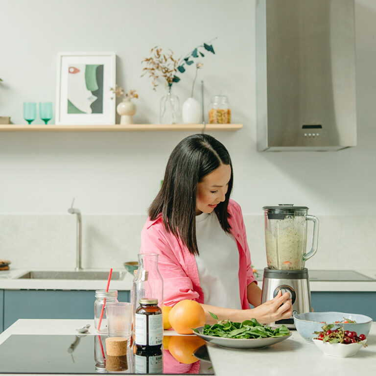 Nutrition : Femme dans sa cuisine devant une table garnies d'aliments sains, qui utilise le mixeur